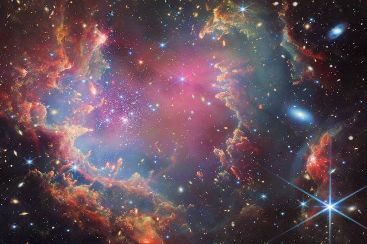 star cluster NGC 602 – Weltraumteleskopfoto eines bunten Nebels mit roten, blauen und violetten Gaswolken und vielen leuchtenden Sternen in der Galaxie.
