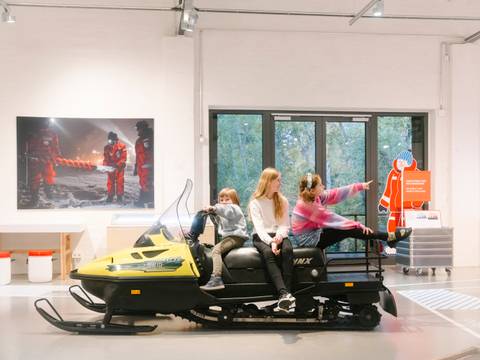 Familienführung "Dünnes Eis" – Drei Kinder sitzen in der Sonderausstellung "Dünnes Eis" auf einem Schneemobil