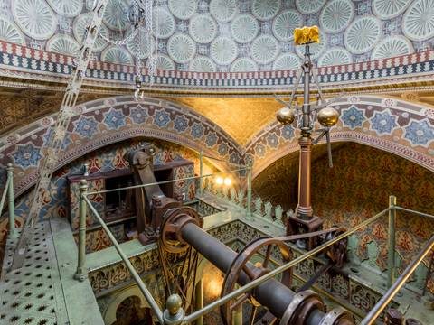 Dampfmaschinenhaus (Moschee), Maschinenraum, oberster Treppenabsatz unter der Kuppel mit Fliehkraftregler und Adler – Maschinenraum des Dampfmaschinenhauses (Moschee) mit kunstvoll verziertem Gewölbe und Metallgestänge. Dampfmaschine in der Mitte. Reiche Muster und Ornamente bedecken Wände und Decke.