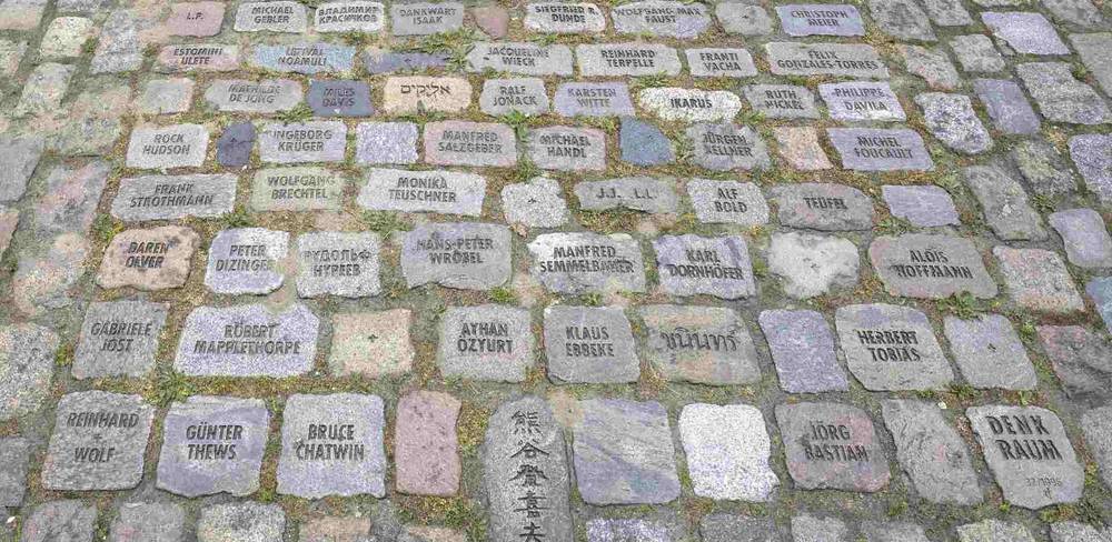 Tom Fecht, Mémoire nomade – Offenes Quadrat I, Detail, 1996-2017 – Pflastersteine mit Namen darauf platziert in einem Gehweg-Muster. Einige Namen: Ralf König, Rock Hudson, Klaus Ebsche und Jörg Bastian.