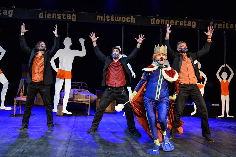Drei maskierte Personen mit erhobenen Armen. Eine Person im blauen Kostüm mit Krone und rotem Umhang. Worte oben: dienstag, mittwoch, donnerstag.