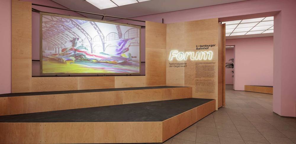 Ausstellungsansicht “Forum Hamburger Bahnhof“, Hamburger Bahnhof - Nationalgalerie der Gegenwart, 2023 – Große Projektionswand mit abstraktem Bild auf Holzpodest. Rechts leuchtet Schrift "Hamburger Bahnhof Forum Nationalgalerie der Gegenwart" im Raum.