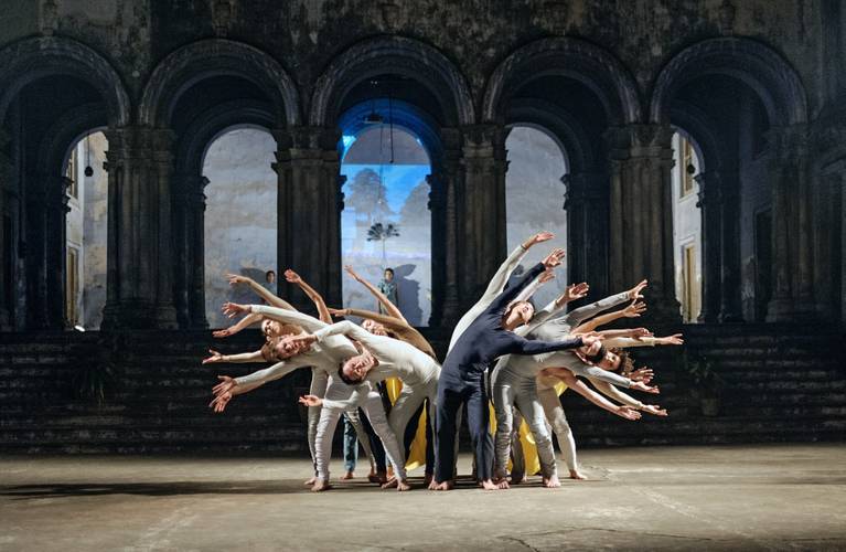“Dialoge 2013 – Kolkata”, Sasha Waltz & Guests – Tanzensemble in synchron gebogener Pose in einer historischen Halle mit beleuchtetem Hintergrund.