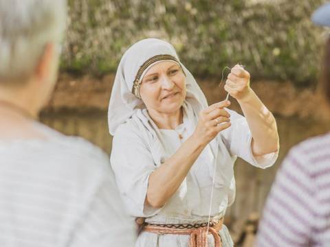 Spinnen mit der Handspindel – Eine Frau in Gewandung mit einem gespannten Wollfaden in der Hand während einer Vorführung im Museumsdorf Düppel