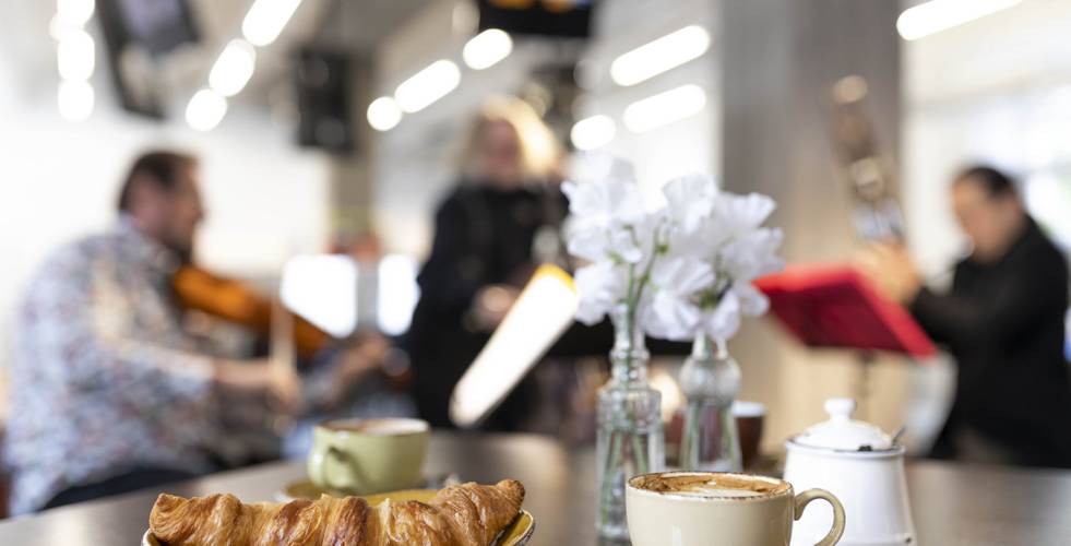 Croissant und Kaffee auf einem Tisch, im Hintergrund spielen Musiker