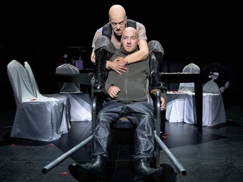 Wallenstein – Eine glatzköpfige Person mit wütendem Gesichtsausdruck nimmt einen erschreckt wirkenden Mann von hinten in die Klammer