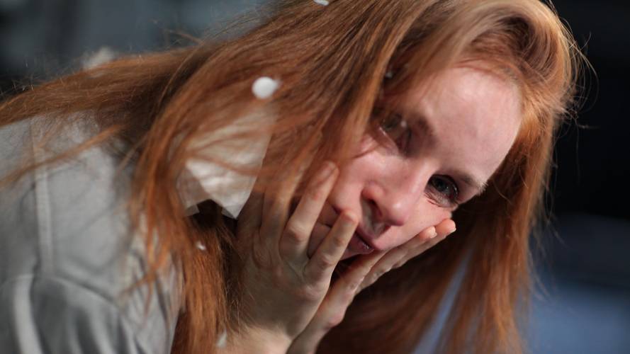 Person mit roten langen Haaren haelt Gesicht mit beiden Haenden. Einige Schaumflocken sind im Haar und auf Kleidung sichtbar.