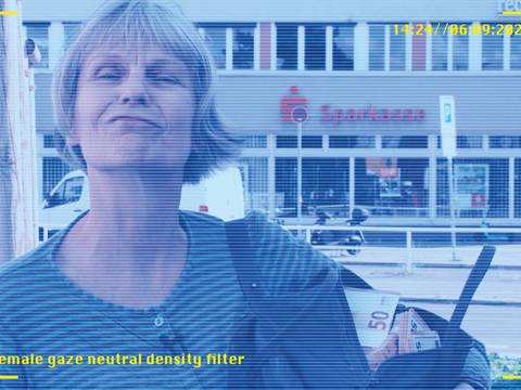  – Eine Person mit kurzen Haaren vor einer Sparkasse. In der Hand Geld mit der Zahl 50. Text: female gaze neutral density filter, 14:24//06.09.2025.