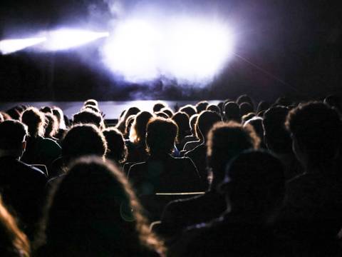  – Menschenmenge sitzt in der Dunkelheit, Lichtstrahlen beleuchten einen Bereich.