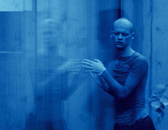 Sasha Waltz & Guests – Person bewegt die Hände vor einer spiegelnden Fläche; das Bild ist blau eingefärbt und zeigt eine verschwommene Spiegelung.