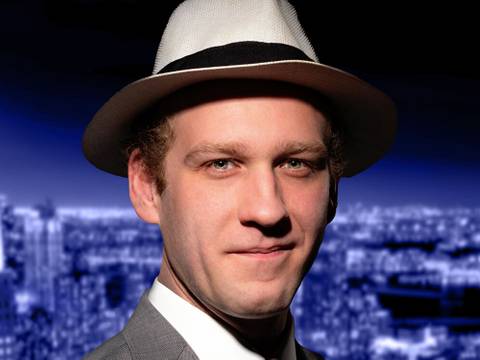 konkursmasse_plakat – Person mit weißem Hut, darauf schwarzes Band. Grauer Anzug. Verschwommene Stadt bei nacht im Hintergrund.