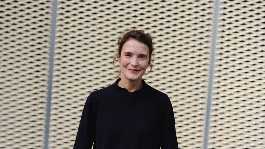 Caterina Lobenstein – Person mit dunklem Pullover vor gelochter Wand mit diagonalem Muster.