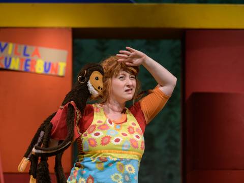 Pippi Langstrumpf – Person mit bunter Kleidung hält einen Affen-Puppe, im Hintergrund ein Schild mit "VILLA KUNTERBUNT".