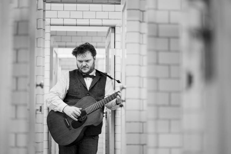 Svavar Knútur – Svavar Knútur mit Gitarre zwischen einem Türrahmen nachdenklich nach unten schauend.