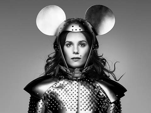  – Person in gepunkteter Rüstung mit Mickey-Maus-Ohren-Helm, neutraler Gesichtsausdruck, welliges Haar, schwarz-weiß Bild.