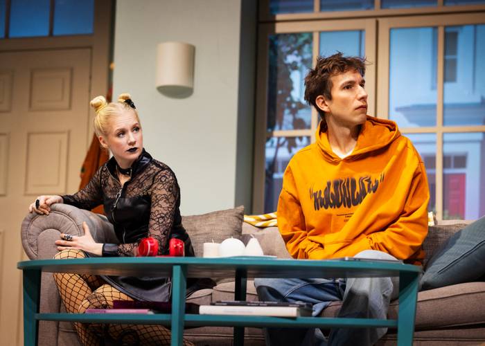 Freundlich oder schwierig? Von li.: Stefanie Darnesa und Mathias Renneisen. – Zwei Personen sitzen auf einem Sofa. Links eine Blondine in schwarzem Spitzenoberteil, rechts eine Person im orangen Hoodie mit Schriftzug „WEKULPUTS“.