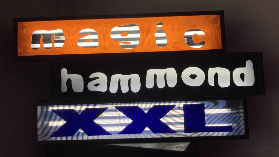 Leuchtkasten mit den Woertern "magic" (orange Hintergrund), "hammond" (schwarz Hintergrund), "XXL" (blau auf Streifendesign).
