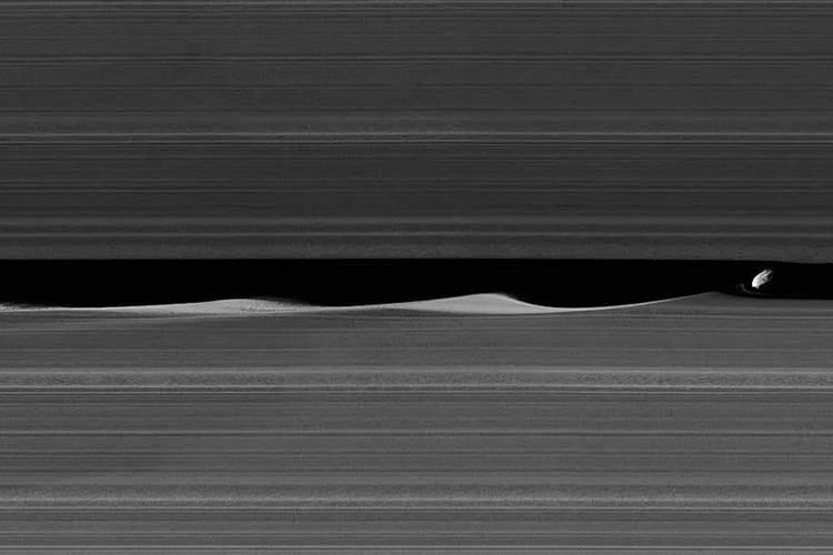 Der kleine Saturn-Mond Daphnis schlägt auf seiner Bahn Wellen in die Ringe des Saturns. – Aufnahme aus dem Weltraum mit Saturn-Ringen und Saturn-Mond.