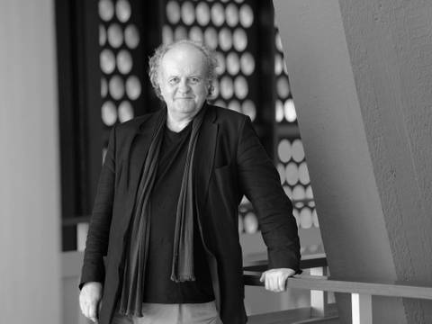 Der Komponist Wolfgang Rihm 2021 in der Philharmonie Berlin – Ein Mann in Jacke und Schal lehnt an einem Geländer im Foyer der Philharmonie.