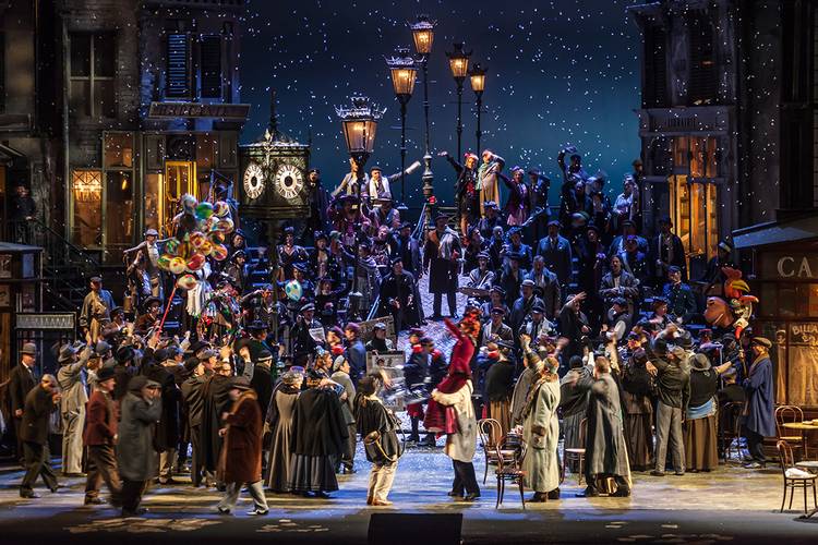 La Bohème – Große Menschenmenge auf einer verschneiten Theaterbühne mit Laternen, Ballons, verkleideten Personen; Schilder: BRIGANDS, LIBRAIRIE, CAFE.