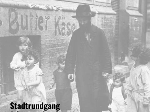 Stadtrundgang zum Scheunenviertelpogrom 1923 – Mann mit Bart und Hut geht mit vier Kindern auf Bürgersteig entlang. An der Wand Schriftzug Butter Käse. Text unten links: Stadtrundgang Scheunenviertelpogrom.