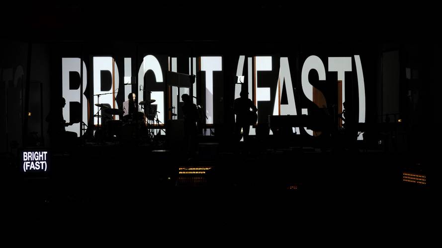 Stereophonic – Silhouetten von Musiker*innen vor einer großen Leinwand mit der Aufschrift: BRIGHT (FAST). Links kleinerer Bildschirm, gleiche Aufschrift.