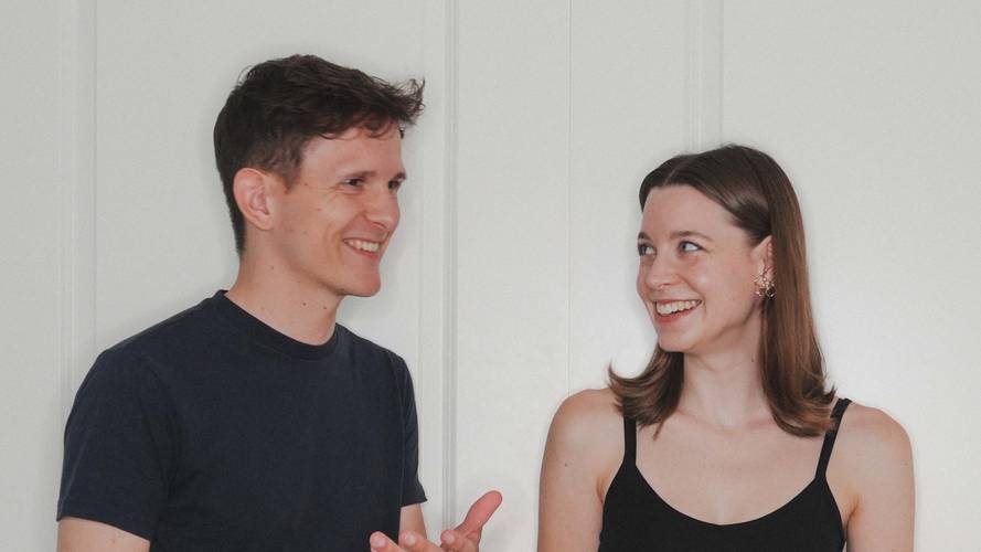 Zwei lachende Personen; links eine Person mit dunklem T-Shirt, rechts eine Person mit schwarzem Top und auffälligem Ohrring.
