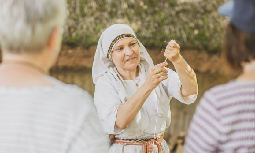 Spinnen mit der Handspindel – Eine Frau in Gewandung mit einem gespannten Wollfaden in der Hand während einer Vorführung im Museumsdorf Düppel