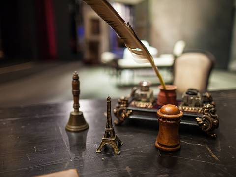Backstage-Führung – Eine Feder steht in Tinte auf einem dekorativen Holzstift, daneben Eiffelturm-Miniatur und zwei Briefbeschwerer auf einem alten Schreibtisch.