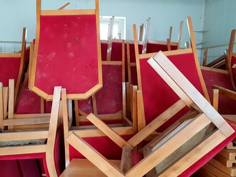 Stühle des Zentralen Runden Tisches (rechts) und Polstersessel der Volkskammer (links) in Einlagerungssituation vor 2019 – Rote Stühle mit Holzrahmen sind in einem Raum gestapelt. Die Stühle sind kopfüber aufeinander gestellt.