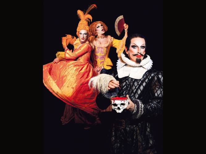 PINK GRIMM: Shakesqueer – God save the Queens – Drei Personen in bunten historischen Kostümen, zwei tragen orange Kleider, eine in schwarz-weißem Gewand hält einen Schädel mit rotem Detail.