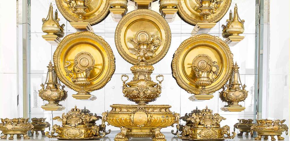 Das große Silberbuffet aus dem Rittersaal des Berliner Schlosses, Detail, Goldschmiedewerkstatt Biller, Augsburg, 1695-1698 – Goldene Tischdekoration auf Glasregalen: Große Teller, Krüge und Verzierungen. Zentrale Schale mit zwei Henkeln und filigranen Details.
