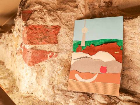 Strategrafie im PETRI Berlin – Collage mit Landschaft in warmen Farben auf historischem Mauerwerk aufgehängt. Gezeichnete kugelförmige Struktur auf blauem Hintergrund sichtbar.