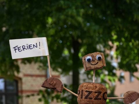 Mit Korkmännchen basteln wir uns durch die Geschichte der Straßennamen. – Ein selbstgebasteltes Korkmännchen schwenkt eine Fahne mit der Aufschrift "Ferien!".