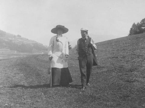Auf der Erde: Alma und Gustav Mahler beim Spaziergang durch die Wiesen über Toblach im dunklen Sommer 1909 – Mann und Frau spazieren über Hügel