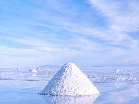  – Ein Salzberg pyramidenförmig in spiegelnder Salzebene. Wolkiger Himmel oben. Mehrere kleinere Salzberge im Hintergrund.