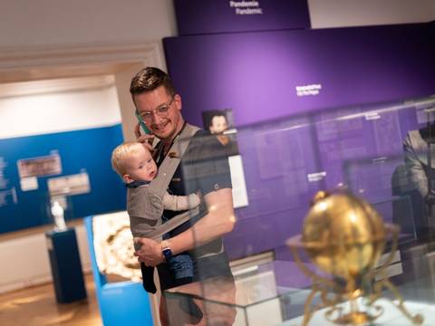 Besucher mit Baby im Ephraim-Palais. – Ein Mann mit Baby im Tragetuch und einem Audioguide am Ohr in der Ausstellung BerlinZEIT