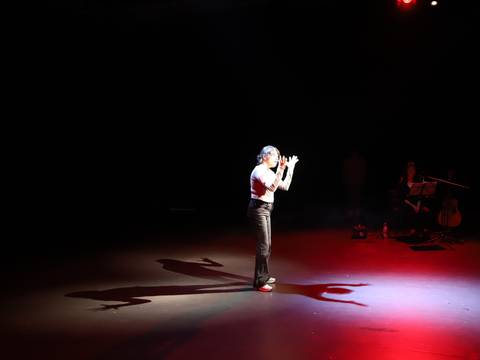  – A person signing on stage in a red and white beams of lights which creater 2 shadows behind the person on the floor and one shadow in front of them.