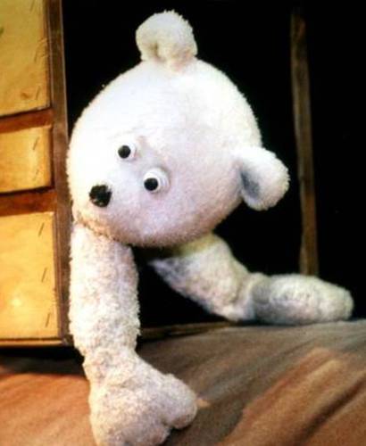 Weißes Plüschtier, das einem Eisbären ähnelt, schaut mit schiefem Kopf aus einer geöffnete Holztür, Augen schielen spielerisch zur Seite.