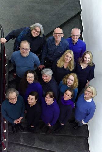 NIE WIEDER! – Vierzehn lächelnde Personen stehen auf einer Treppe, von oben gesehen, einige tragen blaue oder lilafarbene Kleidung.