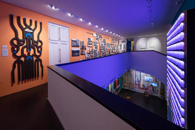 Kunstausstellung mit Wandinstallationen und leuchtenden Röhren. Neonbeleuchtung. Text: "HERE SOME OF US CAN SEE. I AM THE MOST DANGEROUS".