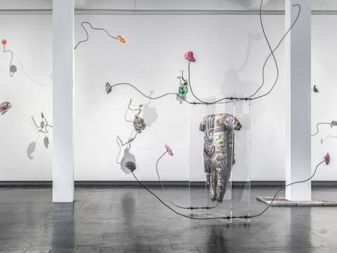 Mariechen Danz, Clouded in Veins, 2021 – Blick in einen Ausstellungsraum, in dem eine Installation aus dünnen, gebogenen Metallstangen zu sehen ist, an die bunte Objekte angebracht sind.