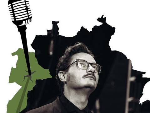  – Männlich-gelesene Person mit Brille, Anzug und Schnurrbart, im Hintergrund ein schwarzes Mikrofon und grüne Karte.