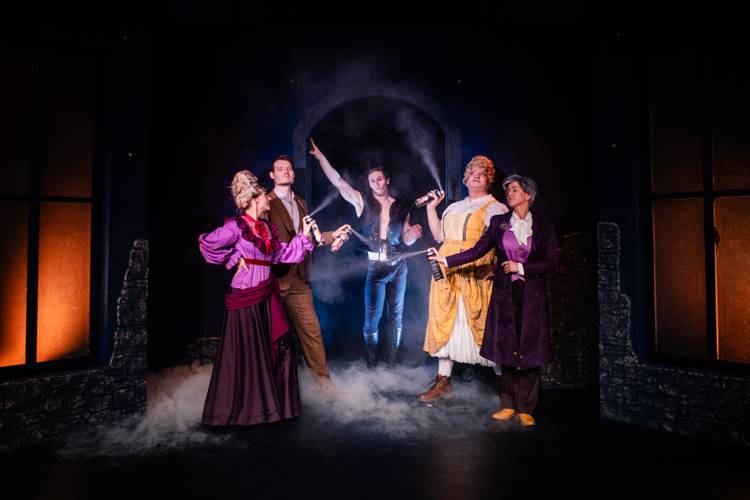 Dracula – A Comedy of Terrors – Fünf Darsteller*innen mit Spraydosen auf der Bühne, von Nebel umgeben. Vier tragen historische Kostüme, die mittlere Person trägt eine Lederweste.