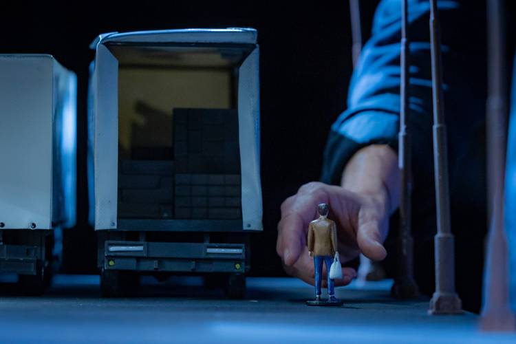 Transport: Cargo – Zwei Miniatur-LKW mit offener Ladefläche; eine Hand platziert eine kleine Figur mit Tüte davor.