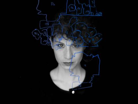 À la carte – Person mit kurzen Locken, das Gesicht zur Haelfte beleuchtet. Blaue Skizze mit Zahlen ueber dem Gesicht auf schwarzem Hintergrund.