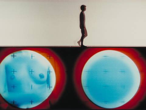 S/N – Screening – Eine Person geht über eine Bühne, unter ihr eine Projektion mit blauen und roten Kreisen.