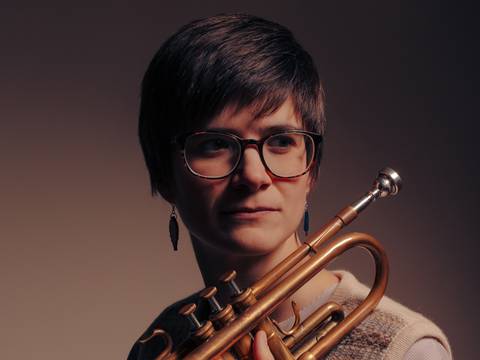 Laura Jurd – Person mit einer Trompete in der Hand vor grauem Hintergrund.