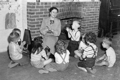 Ruth Crawford Seeger arrangierte nicht nur Folksongs für Kinder, sondern beteiligt sich in den 1940er Jahren auch am Musikunterricht im Kindergarten ihrer Tochter. – Kniende Frau im Kreis von Kindern
