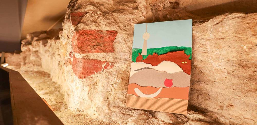 Strategrafie im PETRI Berlin – Collage mit Landschaft in warmen Farben auf historischem Mauerwerk aufgehängt. Gezeichnete kugelförmige Struktur auf blauem Hintergrund sichtbar.